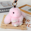 Pink fluffy bunny plush keychain hanging from a gold ring on a wooden tray