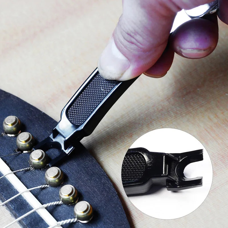 A hand is using a black tool to wind or cut guitar strings, demonstrating a 3-in-1 guitar string winder, cutter, and pin pull
