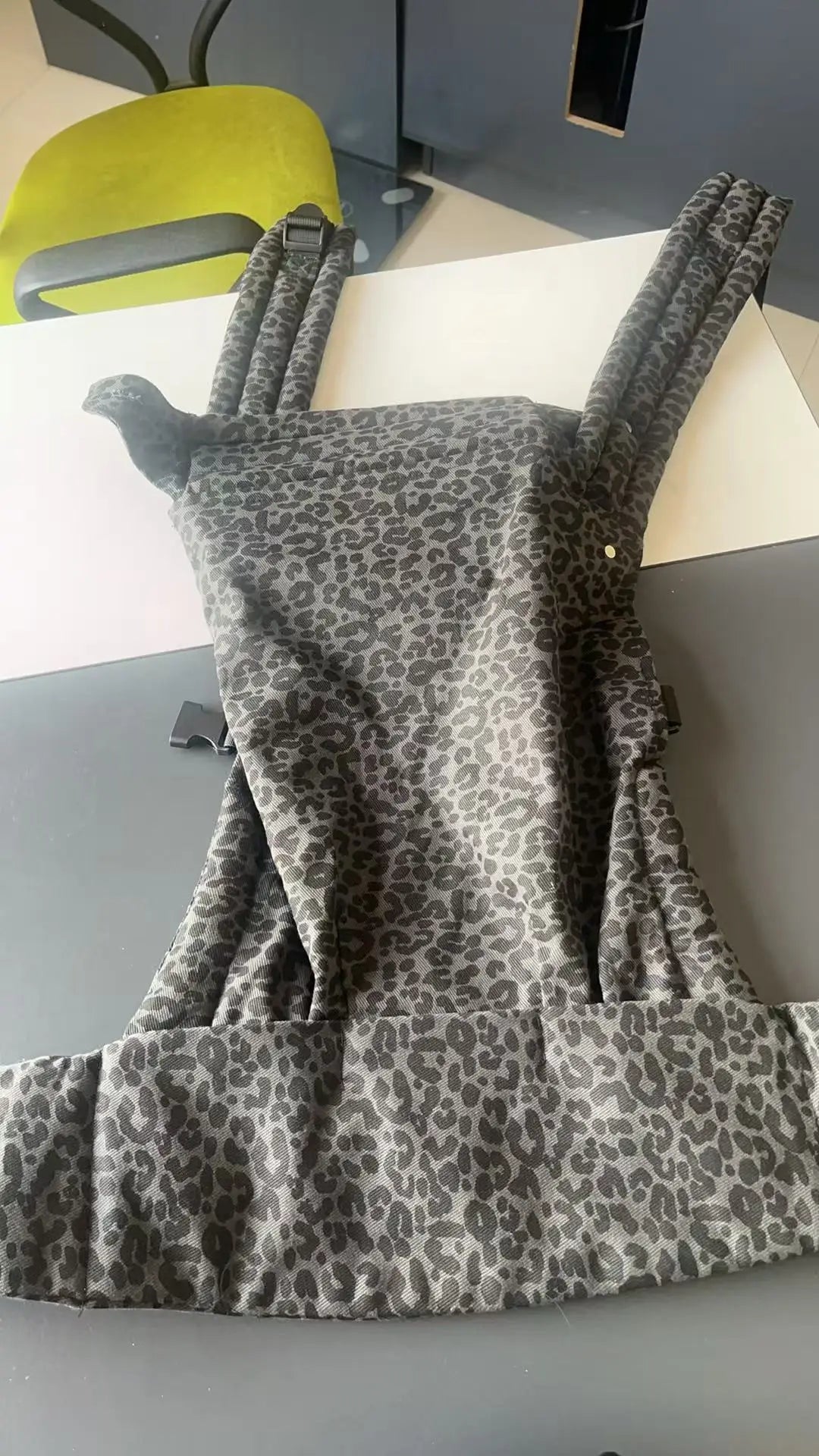A gray leopard print adjustable cotton baby carrier wrap displayed on a table.