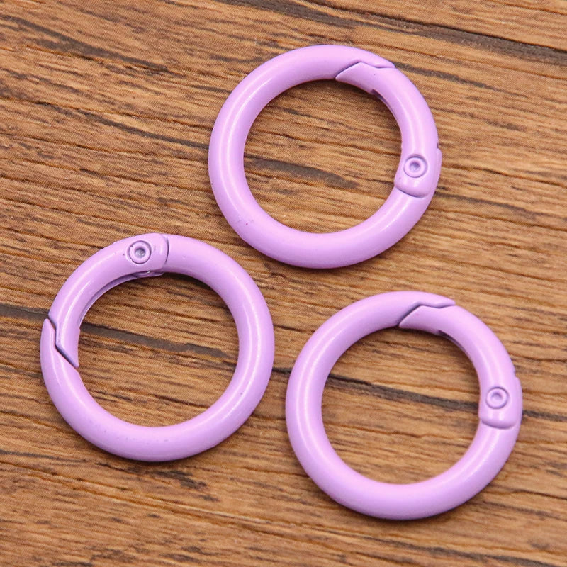 A set of ten purple metal O-ring spring clasps for DIY jewelry and keychains arranged on a wooden surface.