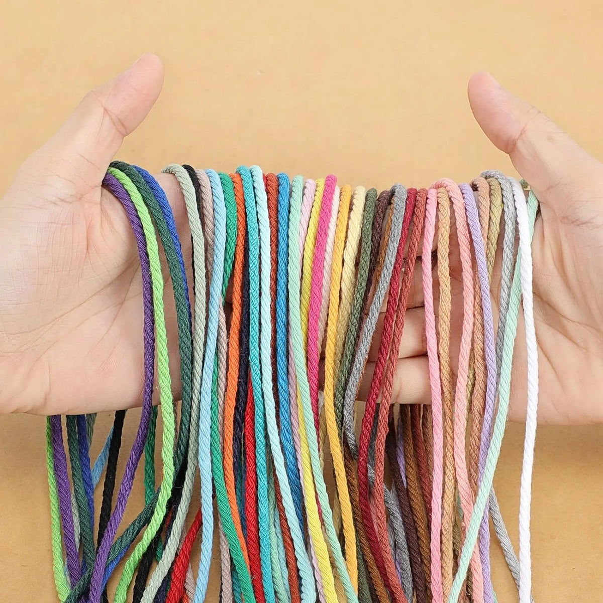 A hand holds a bundle of natural cotton macrame rope in various colors for crafts and decor.