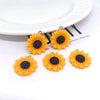 Several bright orange sunflower charms with black centers are displayed on a white plate.