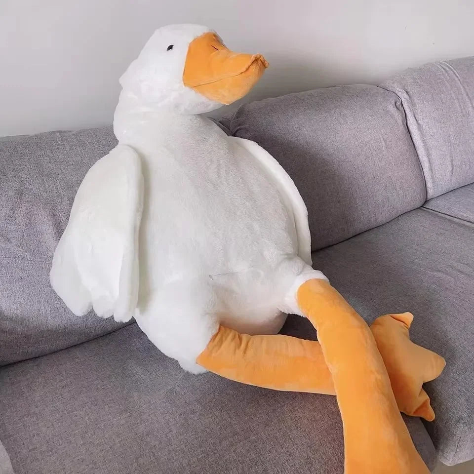 A white goose plush toy with orange beak and legs resting on a gray sofa.