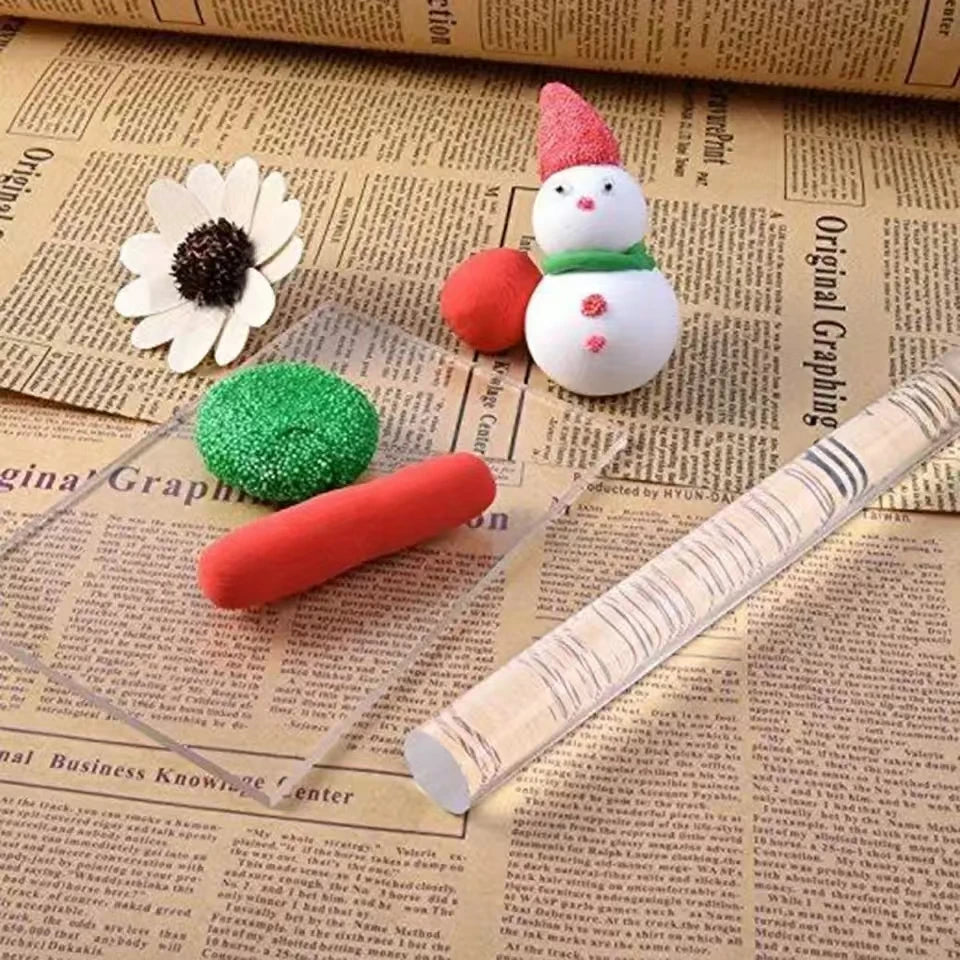 Acrylic clay roller and sheet set with a pink snowman and green clay sphere on parchment paper
