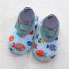 A pair of light blue baby barefoot water shoes decorated with colorful fish patterns and featuring a green strap.