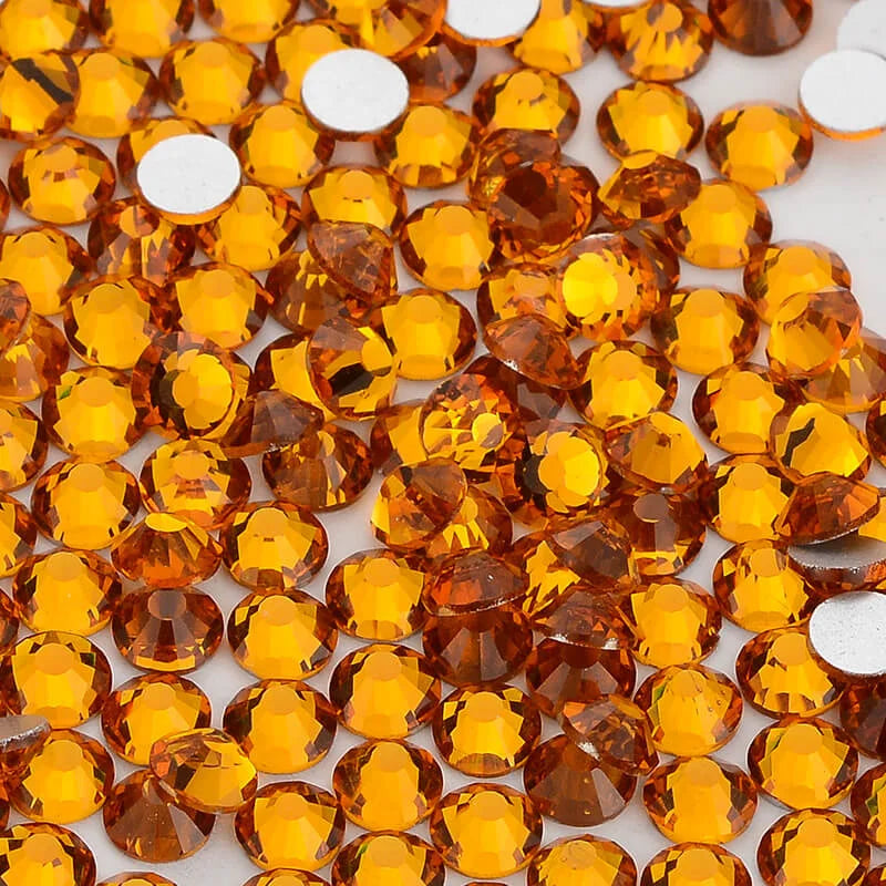 A close-up view of small, round, faceted amber glass crystals used for nail art and crafts.