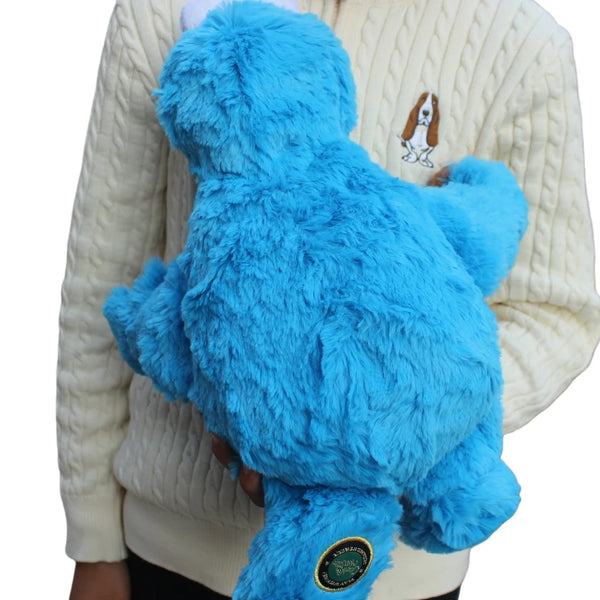 A bright blue Cookie Monster plush toy is held against a person wearing a cream-colored sweater.