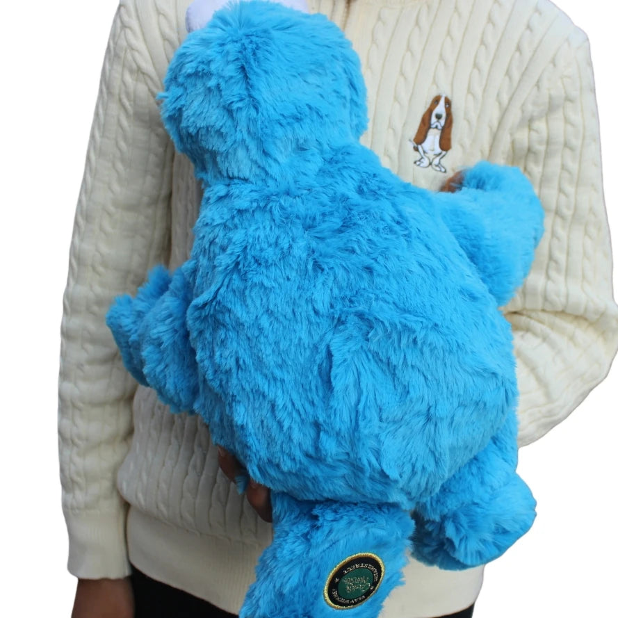 A bright blue Cookie Monster plush toy is held against a cream-colored knitted sweater.