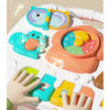 A hand plays a musical piano key on a colorful playmat featuring light-up buttons and hanging toys for babies.