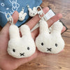 A hand holds a white Miffy cartoon rabbit keychain pendant against a blue fabric background.