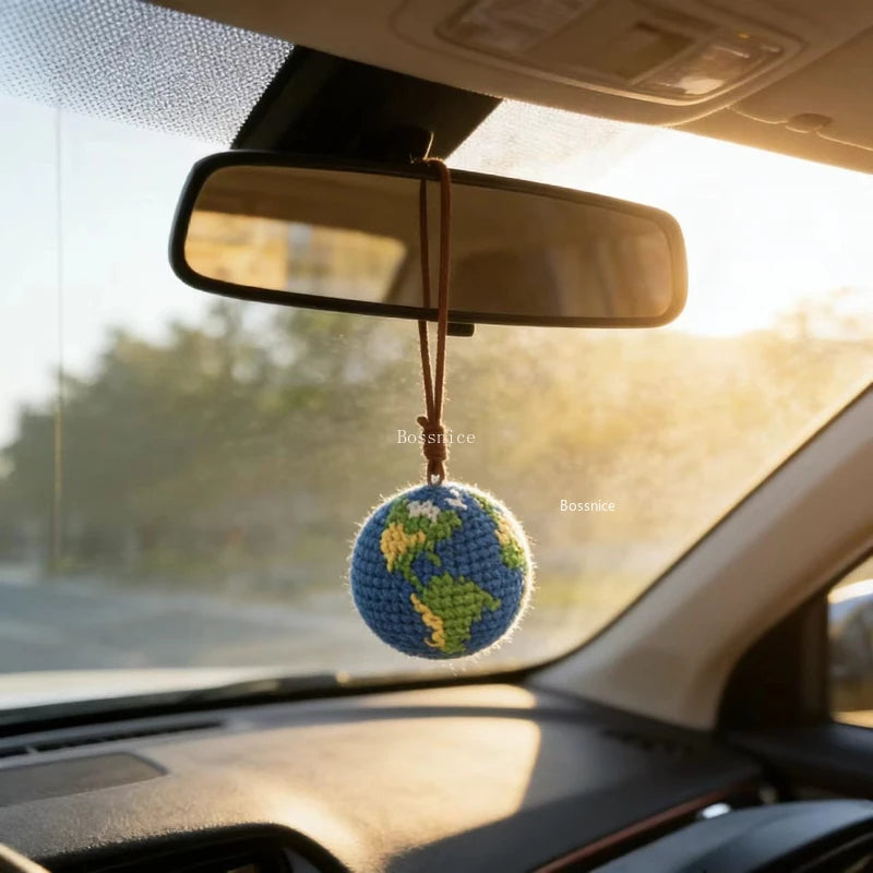 A handcrafted crochet earth keychain charm is suspended from a rearview mirror inside a car.