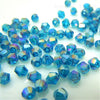 Collection de petites perles de cristal bleues-turquoise facetées éparpillées sur une surface blanche.