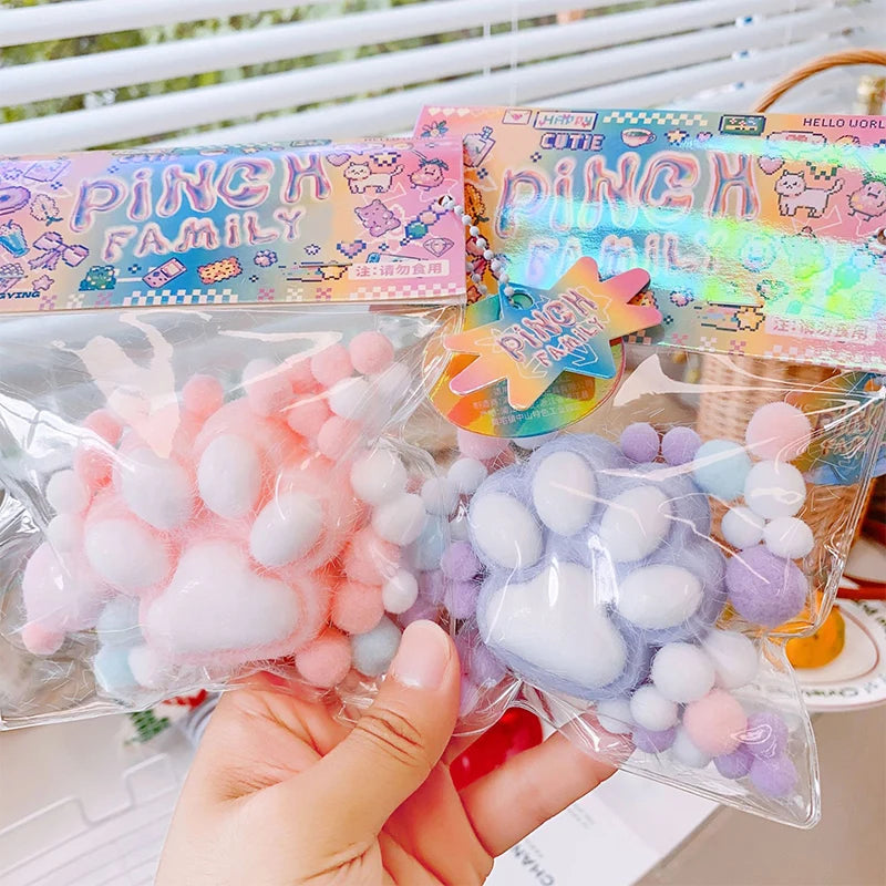 A hand holds a clear plastic bag of pink and purple Kawaii Cat Paw squishy stress relief toys.