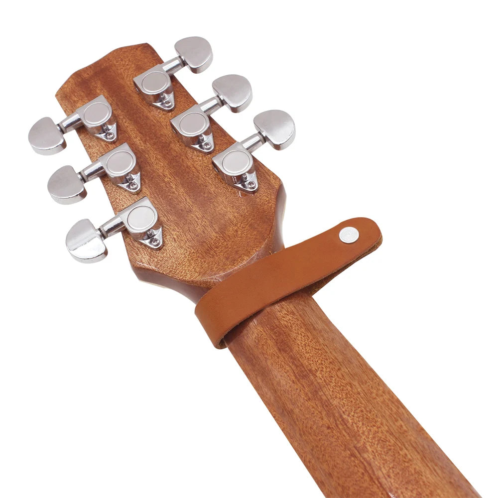 A close-up view of a leather guitar strap button with metal fasteners on a wooden neck piece.