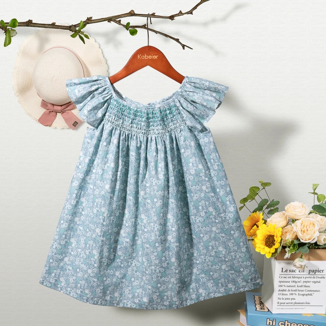 A light blue floral smocked summer dress for girls with ruffled sleeves hanging on a wooden hanger.