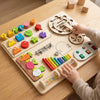 A child's hands interact with a wooden Montessori busy board featuring gears, switches, and sensory elements.