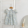 A light blue floral dress with a white Peter Pan collar and bubble sleeves is displayed on a wooden hanger against a white pa
