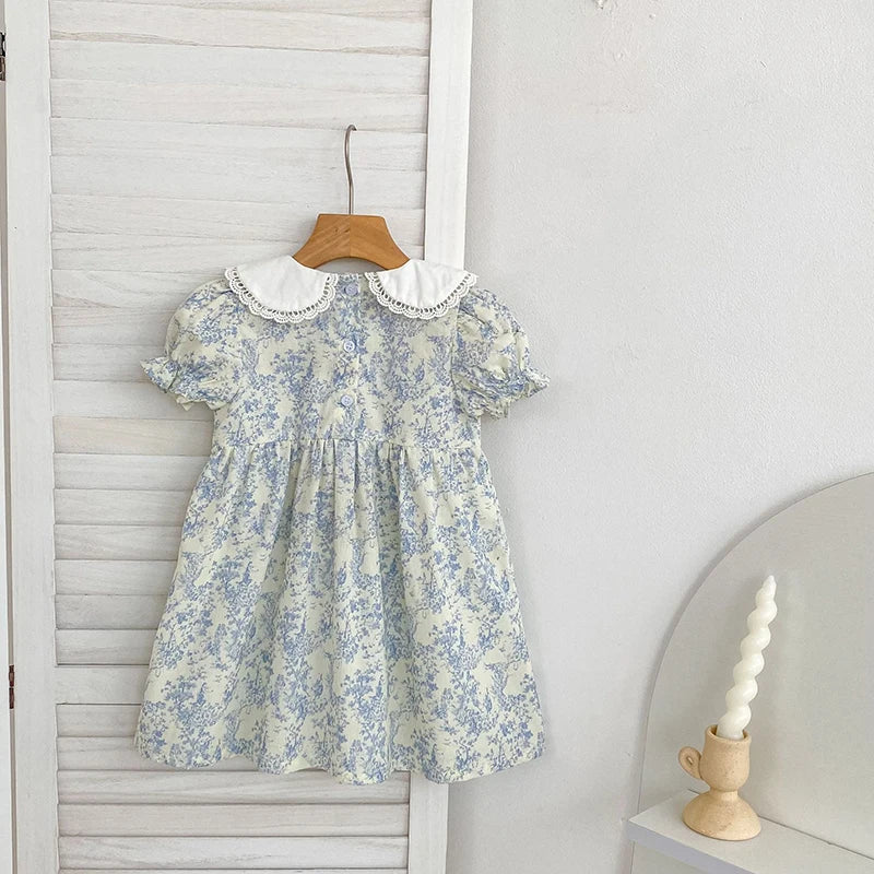 A light blue floral dress with a white Peter Pan collar and bubble sleeves is displayed on a wooden hanger against a white pa