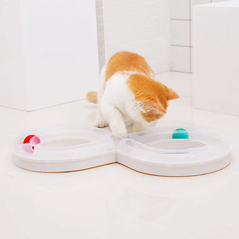 An orange and white cat is interacting with a white plastic interactive toy featuring a tunnel and a green button.