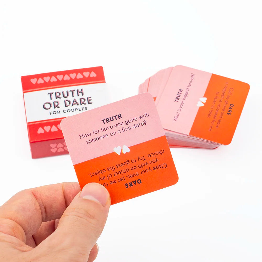 A hand holds an orange Truth or Dare card from a game for couples, with other cards visible in the background.