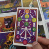 A hand holds a JoJo-inspired tarot card from a deck featuring colored symbols and imagery.