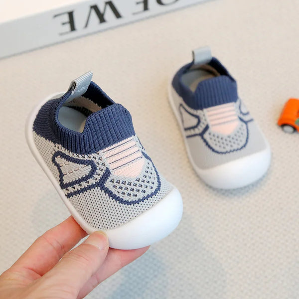 A hand holds a pair of light blue and white breathable mesh baby shoes for summer comfort.