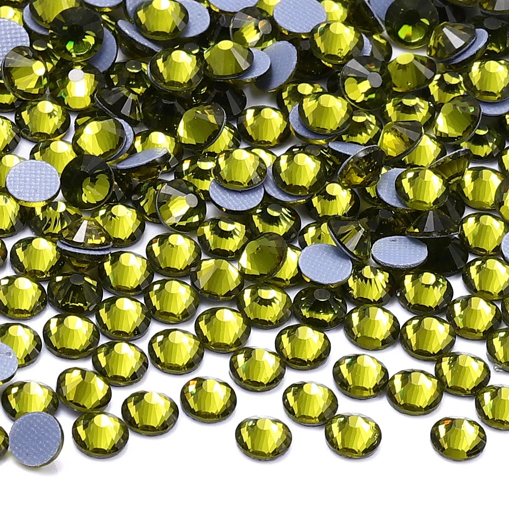 A close-up view of small, faceted glass crystal hot fix rhinestones in various shades of green and gold.