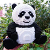 A white and black panda 3D model made of building blocks is held outdoors amidst green foliage.