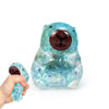 A hand holds a translucent blue dragon fruit bear squishy toy with a brown nose and sparkling inclusions.