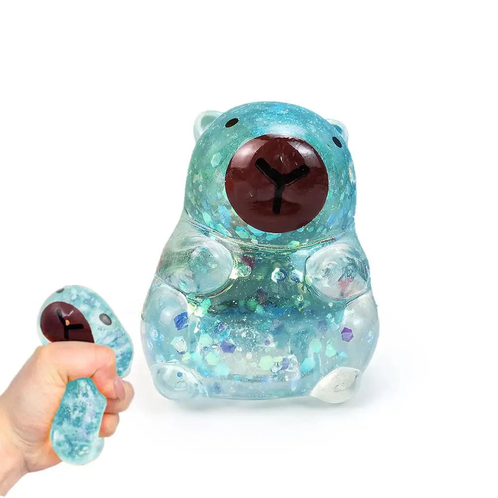 A hand holds a translucent blue dragon fruit bear squishy toy with a brown nose and sparkling inclusions.