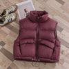 A maroon padded down vest lying on a wooden floor next to a pair of sneakers and a photo frame.