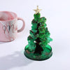 A miniature green Christmas tree with gold star topper and glittery ornaments sits on a clear glass base.