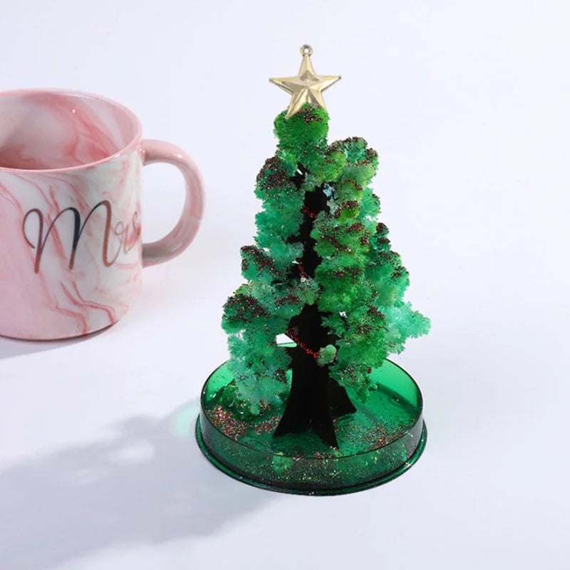A miniature green Christmas tree with gold star topper and glittery ornaments sits on a clear glass base.
