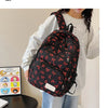 Une femme tient un sac à dos noir avec motif nœud rouge sur un fond clair.