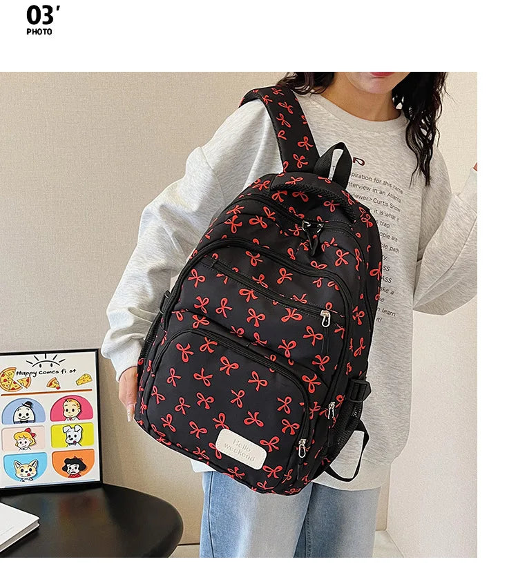 Une femme tient un sac à dos noir avec motif nœud rouge sur un fond clair.