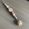 A string of wooden and silicone beads forms a clip for a baby pacifier.