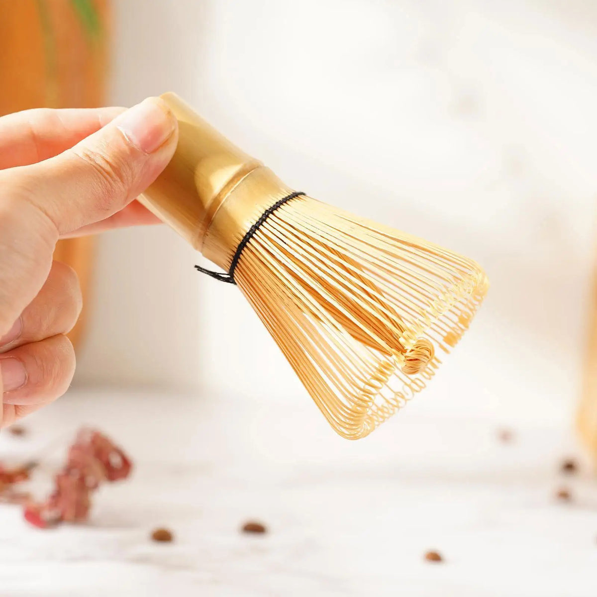 A hand holds a golden bamboo whisk with thin strands for a tea ceremony.