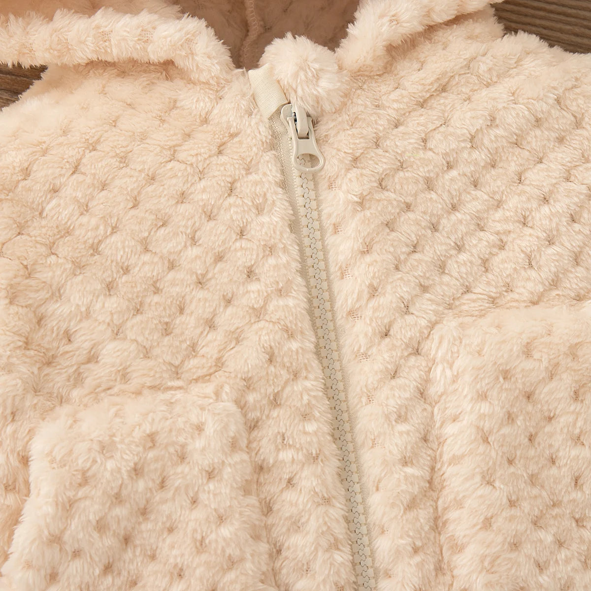 A close-up of a light pink fluffy plush hooded winter jacket with a zipper.