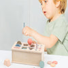 A young child is interacting with a wooden Montessori color and shape sorting box and various colored wooden shapes.