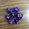 A set of seven polyhedral acrylic dice showing various numbers and colors on a wooden surface.