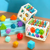 A white cube sorting toy with colored elastic bands and various geometric shapes on a wooden surface.