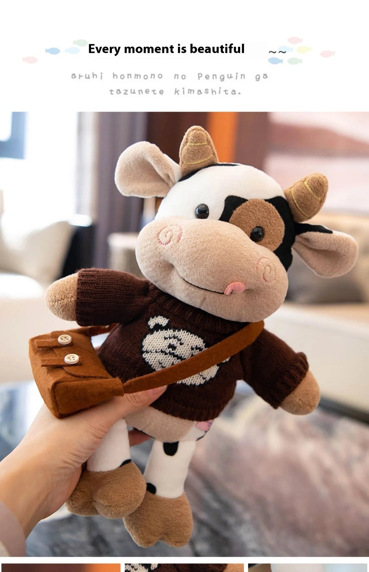 A hand is holding a brown and white plush cow doll with a leather strap.