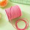 A roll of pink velvet faux suede braided ribbon for crafting and gift wrapping lies on a light green surface.