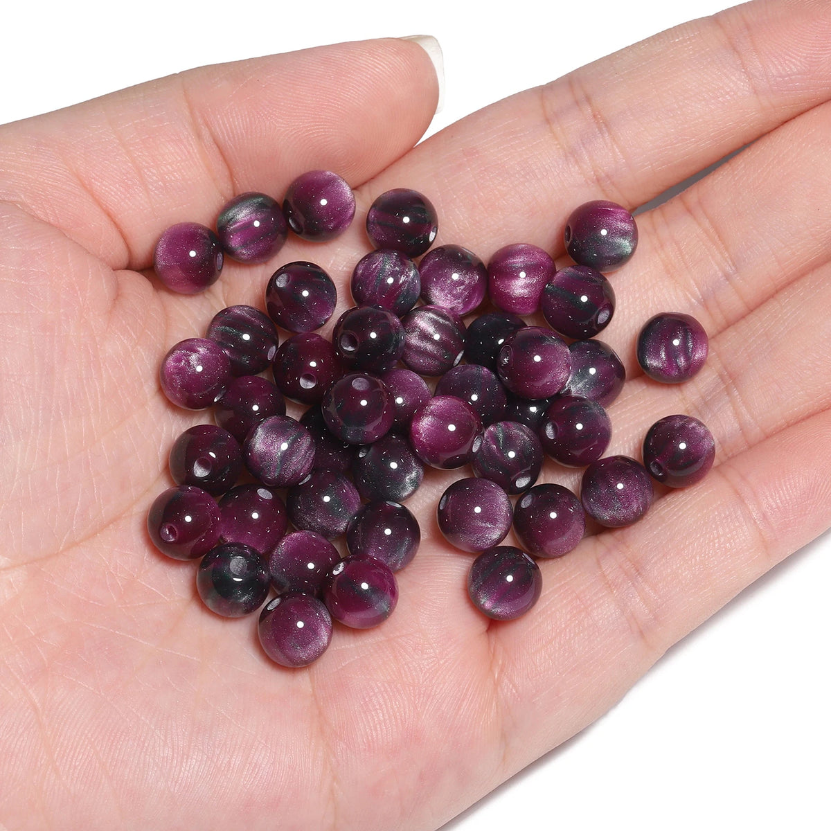 A hand holds a pile of dark purple and reddish-brown tiger eye resin beads for jewelry making.