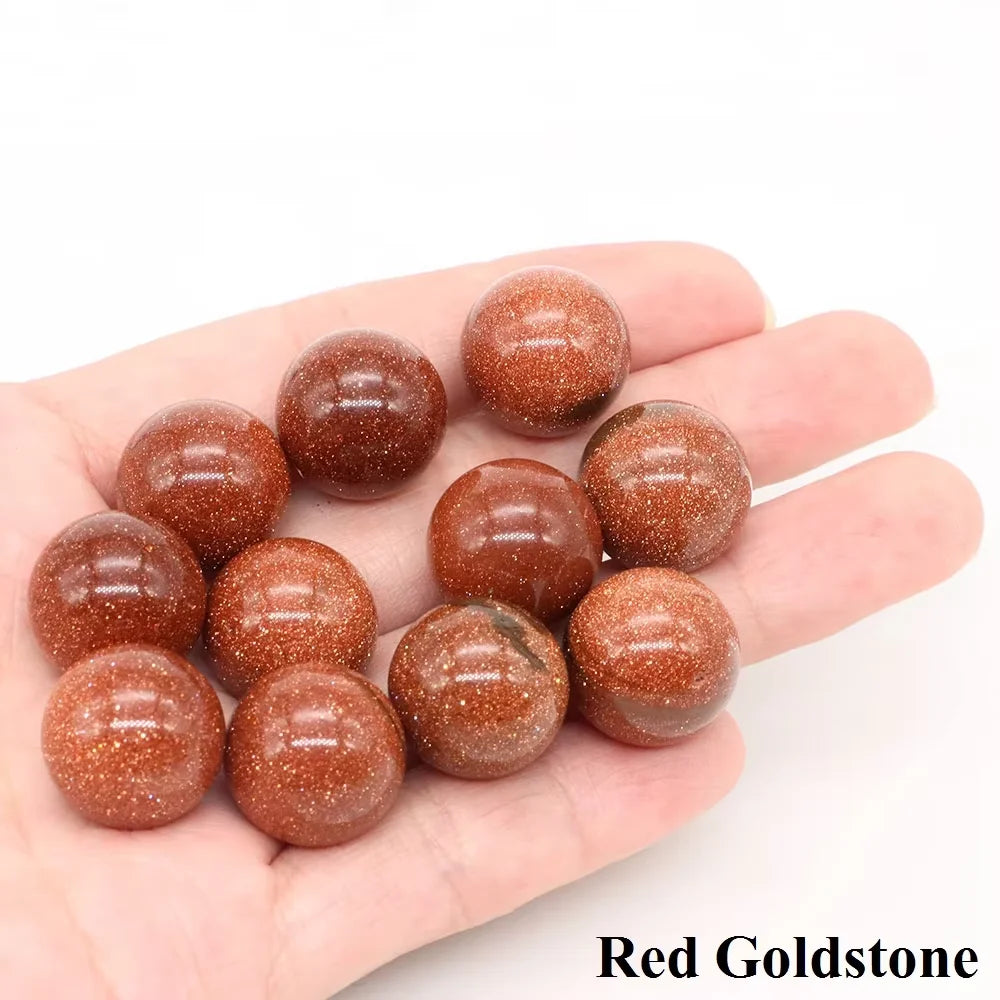 A hand holds several polished reddish-brown Red Goldstone crystal spheres.