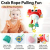 A baby is holding a crab-themed toy with a hanging strap, featuring a silicone rattle and teether.