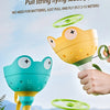 A hand holds a yellow frog-shaped launcher toy, demonstrating the pull string flying saucer for parent-child interaction.