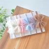 A collection of soft, pastel-colored lace baby rompers and matching headbands arranged on a white surface.