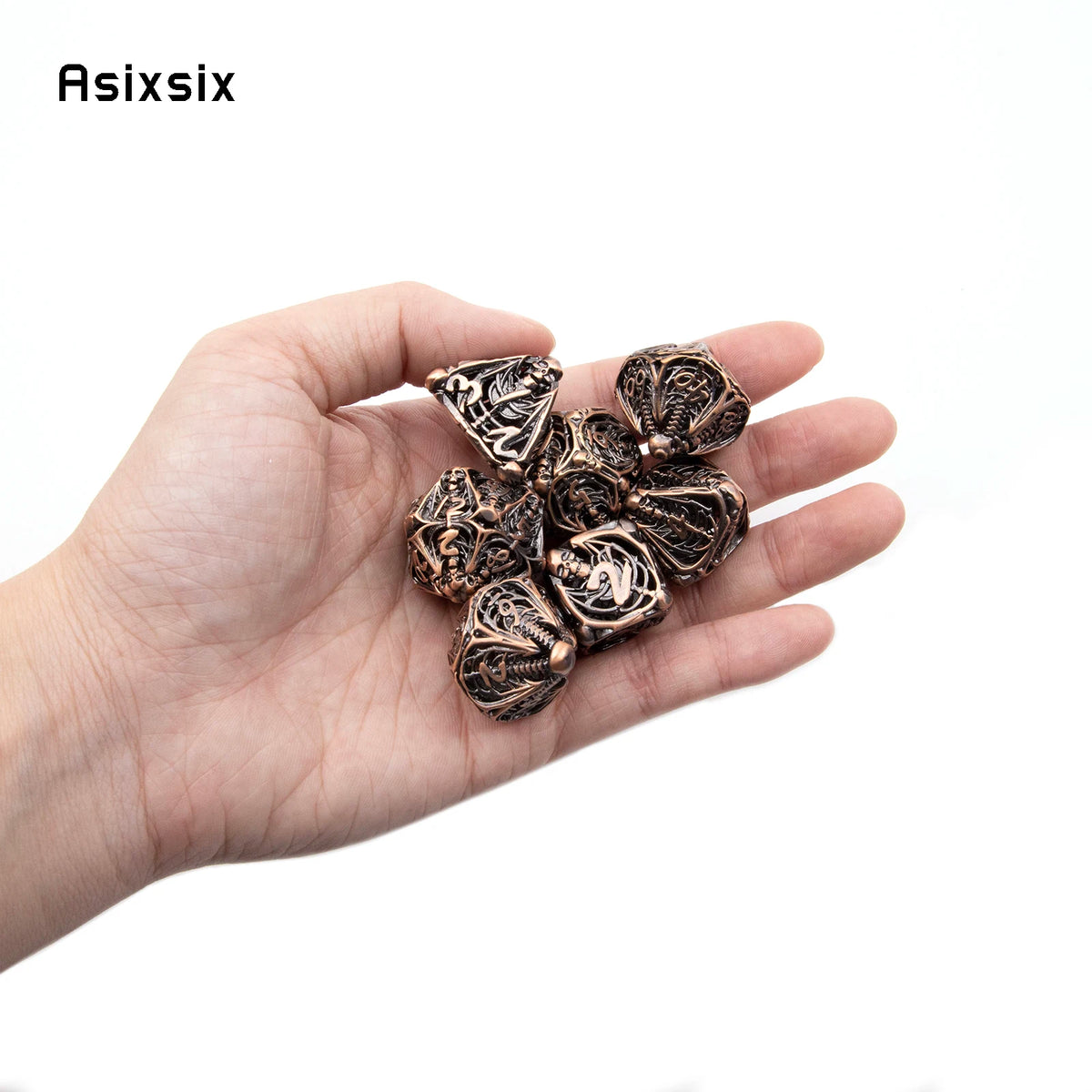 A hand holds a set of coppery skull metal dice for tabletop games.