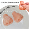 A pink silicone squeeze toy is shown being pinched and squeezed, with two small, translucent spheres on a white plate.
